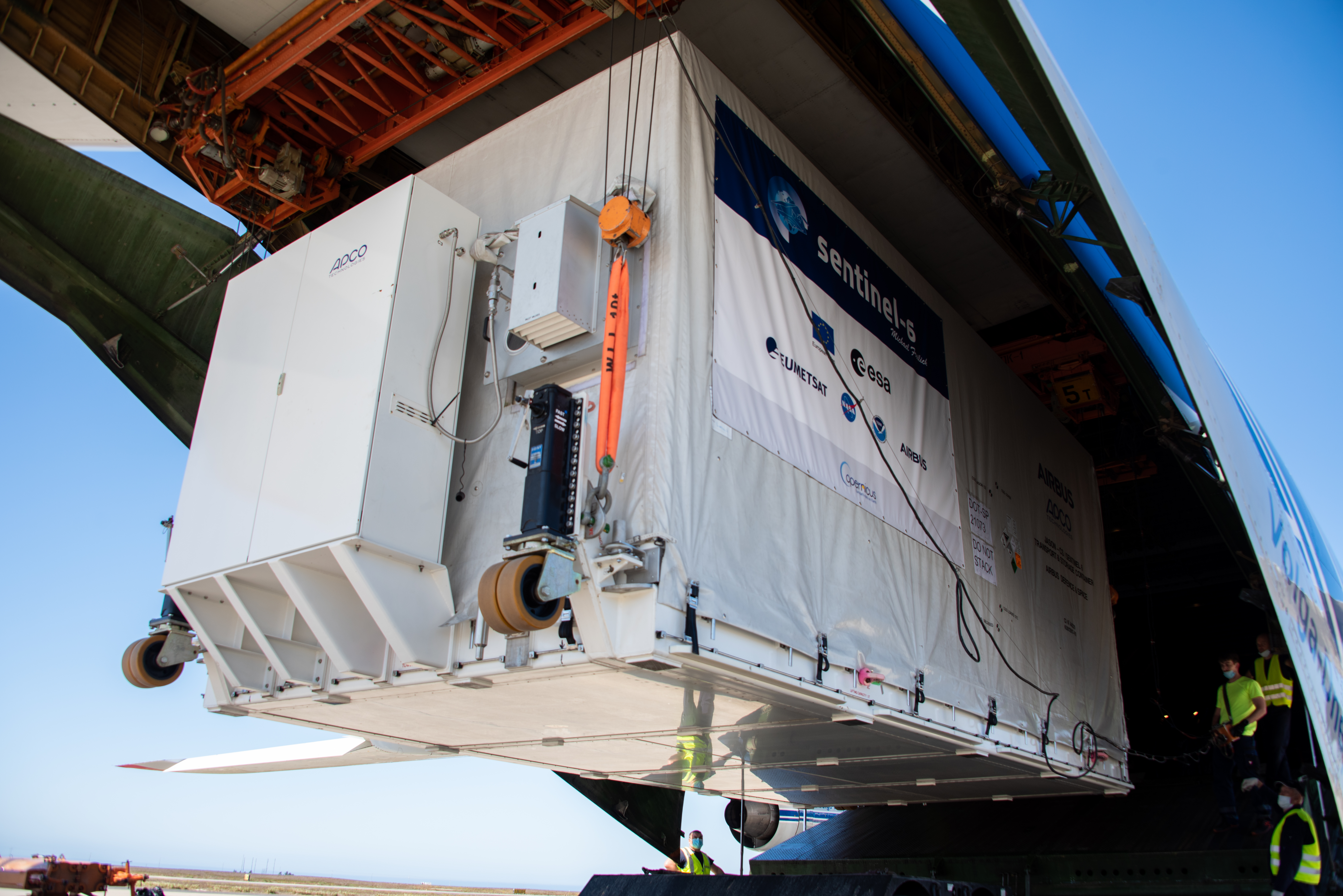 A photo of the spacecraft in its container being lifted out of the plane.